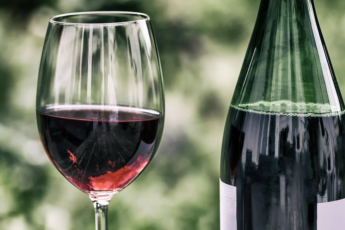Verre de vin rouge rempli et bouteille de vin sur fond végétal flou