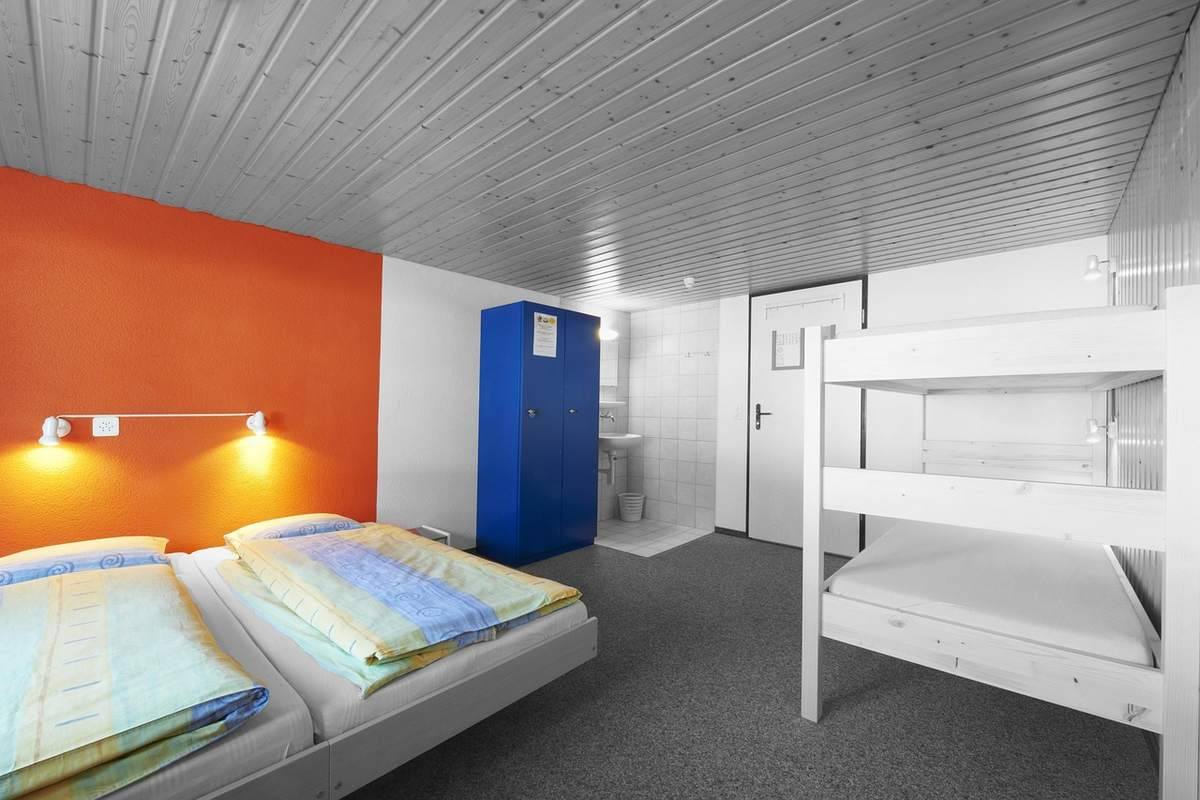 Chambre d'hôtes avec lit double, lit superposé, placard bleu et mur orange Chambre d'hôtes avec lit double, lit superposé, placard bleu et mur orange