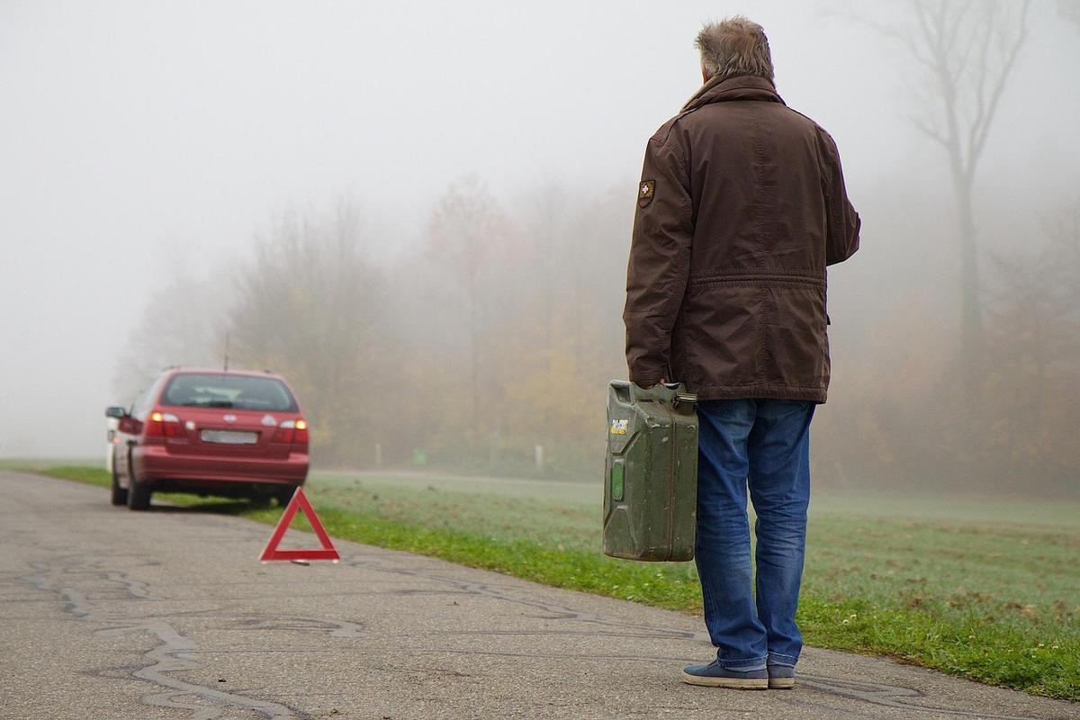 Homme portant un sac près d'une route brumeuse avec une voiture rouge et un panneau triangulaire rouge Homme portant un sac près d'une route brumeuse avec une voiture rouge et un panneau triangulaire rouge