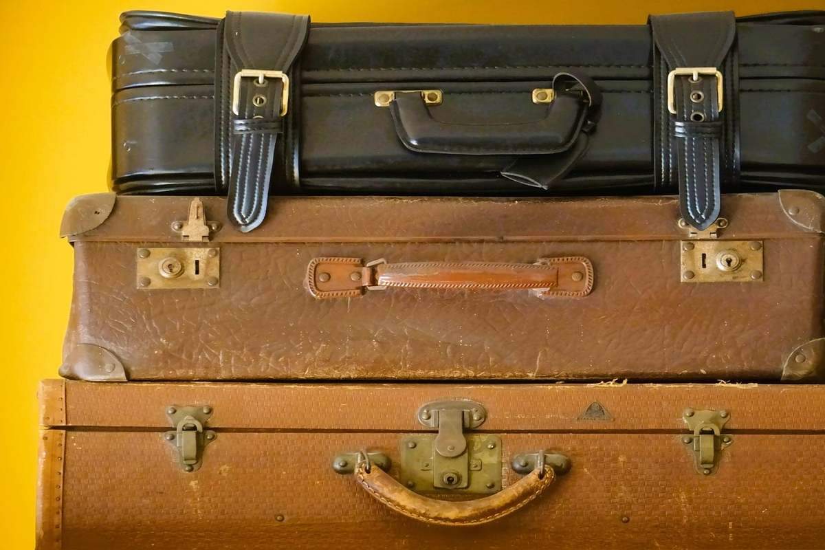 Trois valises vintages empilées en cuir marron et noir sur fond jaune Trois valises vintages empilées en cuir marron et noir sur fond jaune